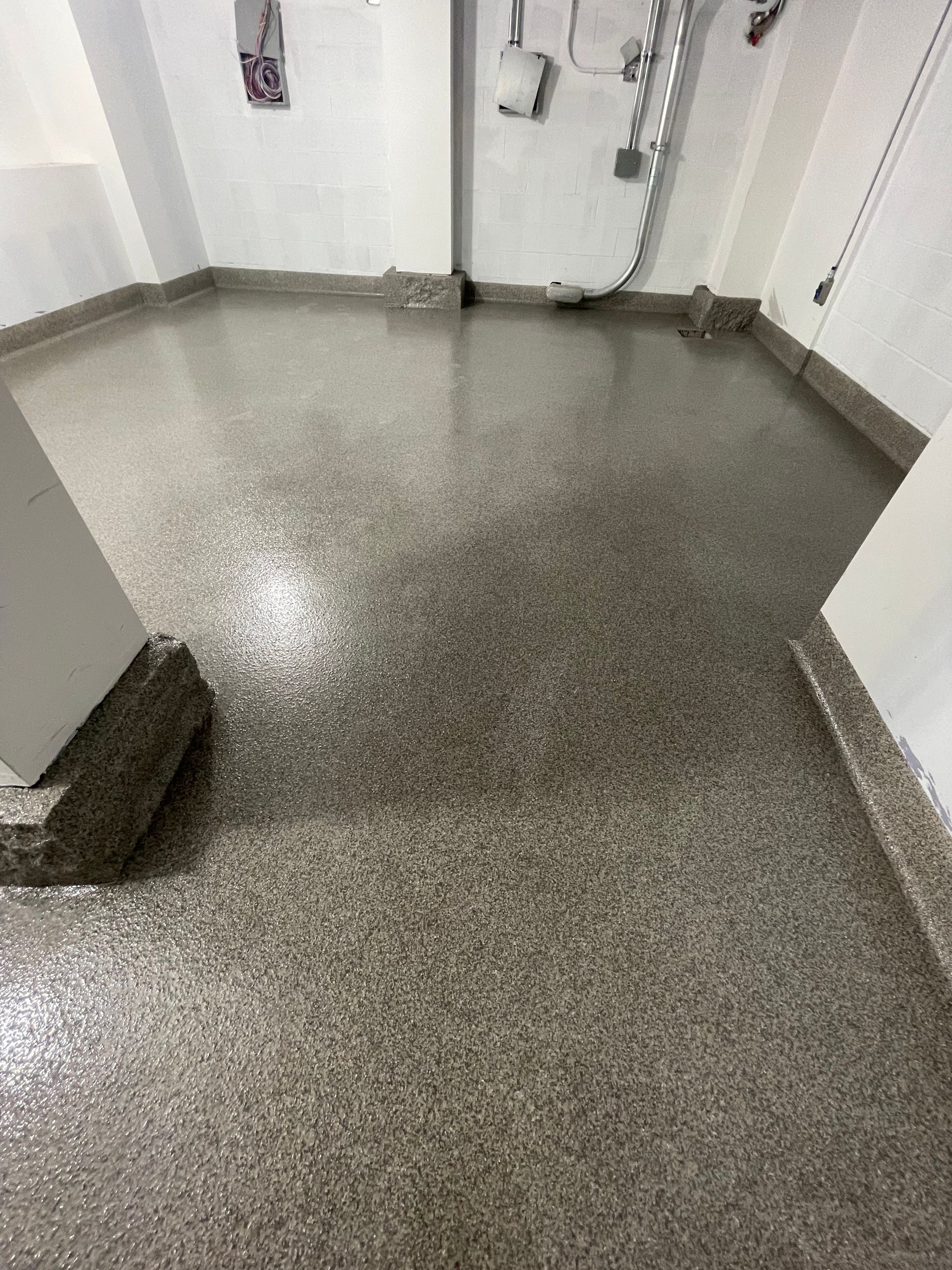 Sol en béton recouvert d'époxy dans une pièce aux murs blancs et à l'encadrement d'une porte. Le sol est gris moucheté.