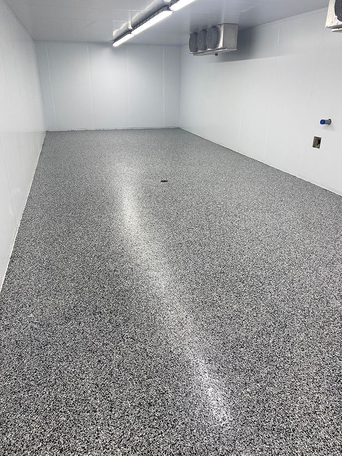 Empty room with a speckled gray floor, white walls and ceiling, and overhead lights.