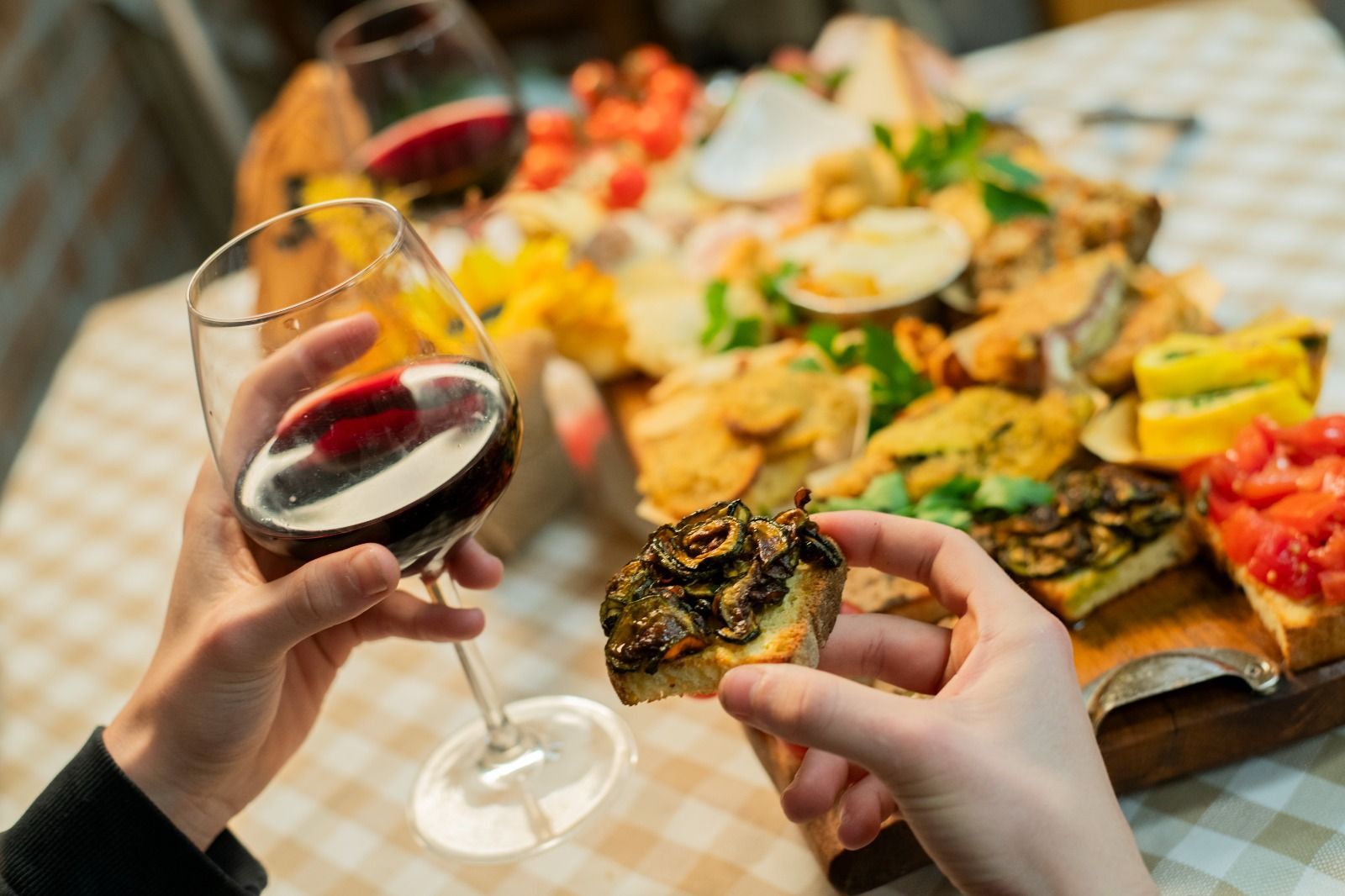 Mani che reggono un bicchiere di vino e del cibo su un colorato tavolo da buffet