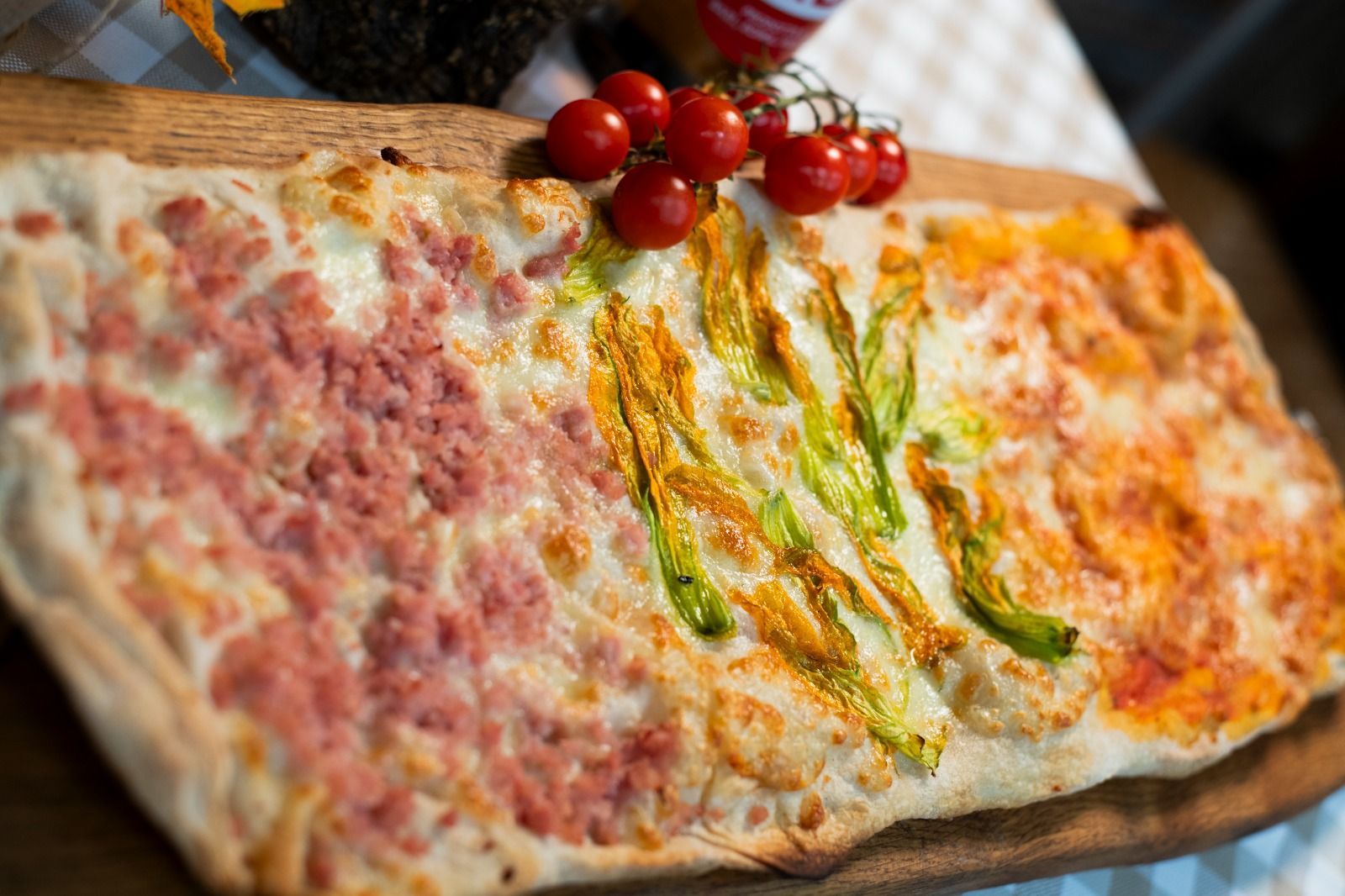 Una focaccia arrotolata e affettata, con ripieno rosa ed erbe aromatiche, guarnita con pomodorini ciliegino e servita su un tagliere di legno.