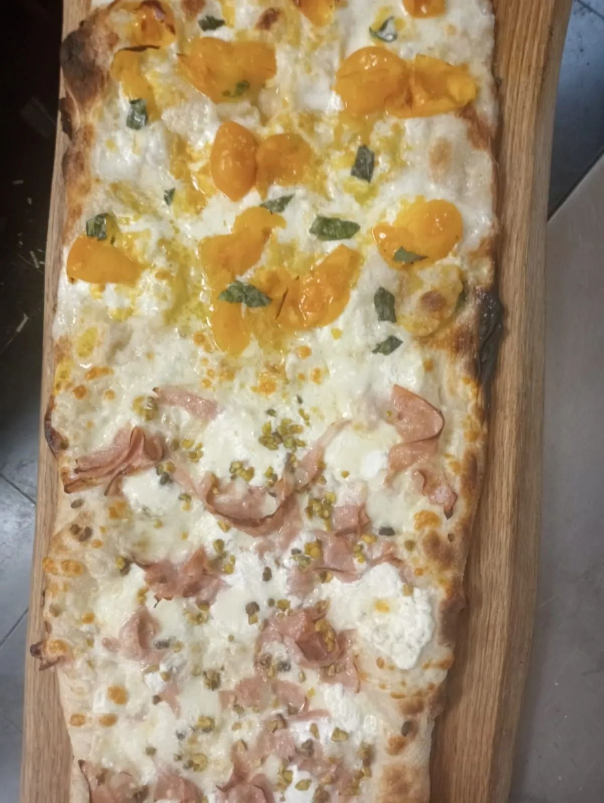 Pizza rettangolare con spicchi d'arancia e prosciutto su un tagliere di legno.