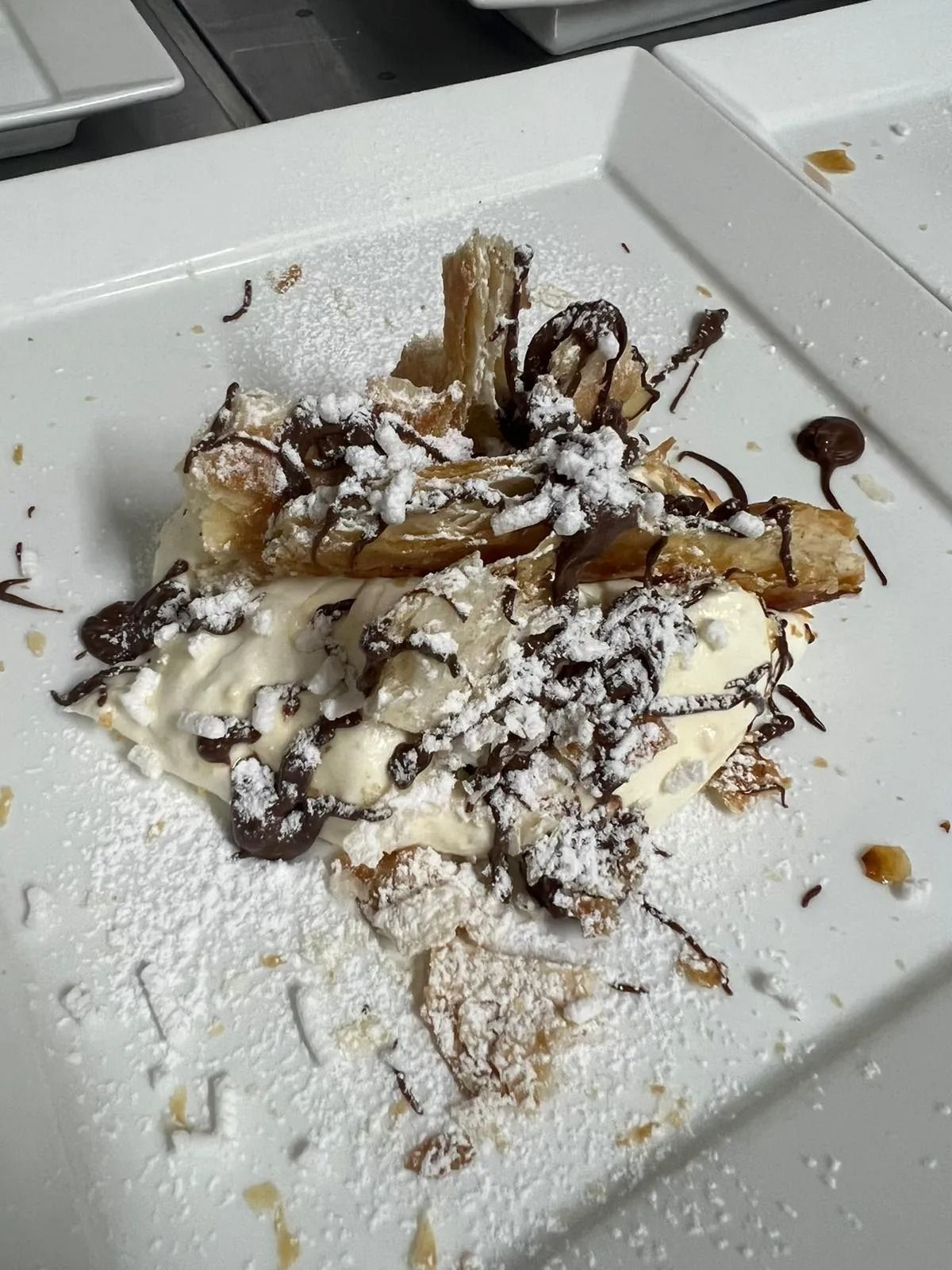 Dessert servito su un piatto bianco, guarnito con zucchero a velo e una colata di cioccolato.