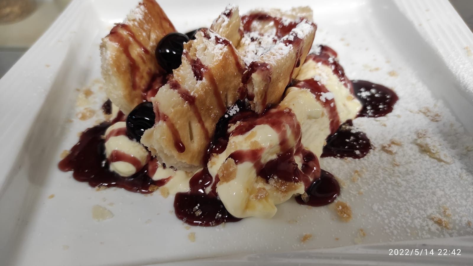 Piatto da dessert con frutta a fette ricoperta di cioccolato fondente e spolverata di zucchero a velo.