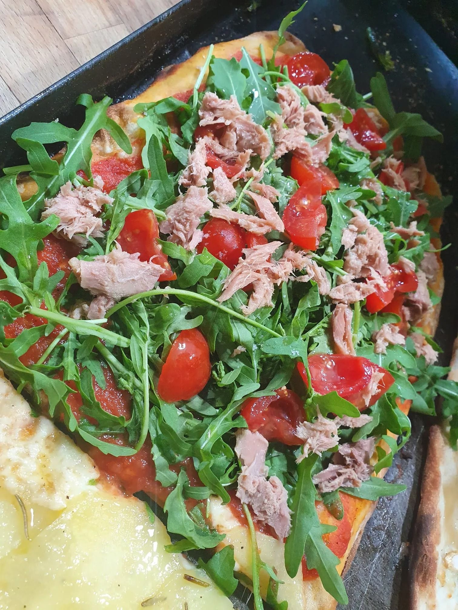 Insalata con rucola, pomodorini, tonno e formaggio grattugiato su un piatto scuro, con pane a bordo.