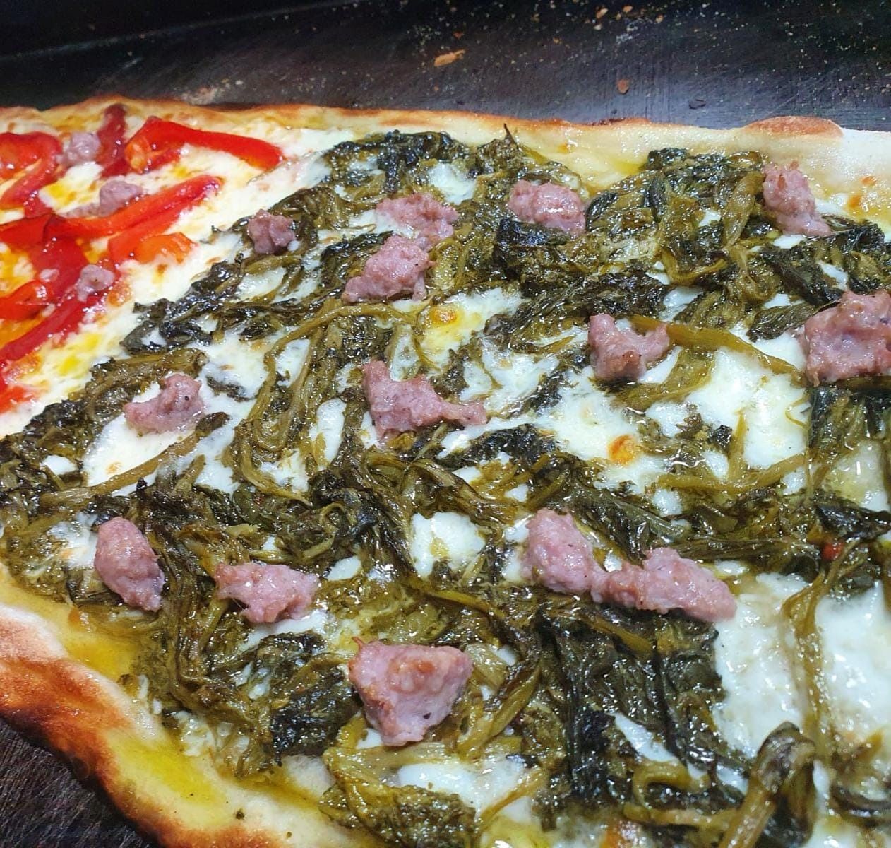 Primo piano di una pizza condita con verdure, formaggio e pezzi di carne, con salsa di pomodoro visibile su un lato.