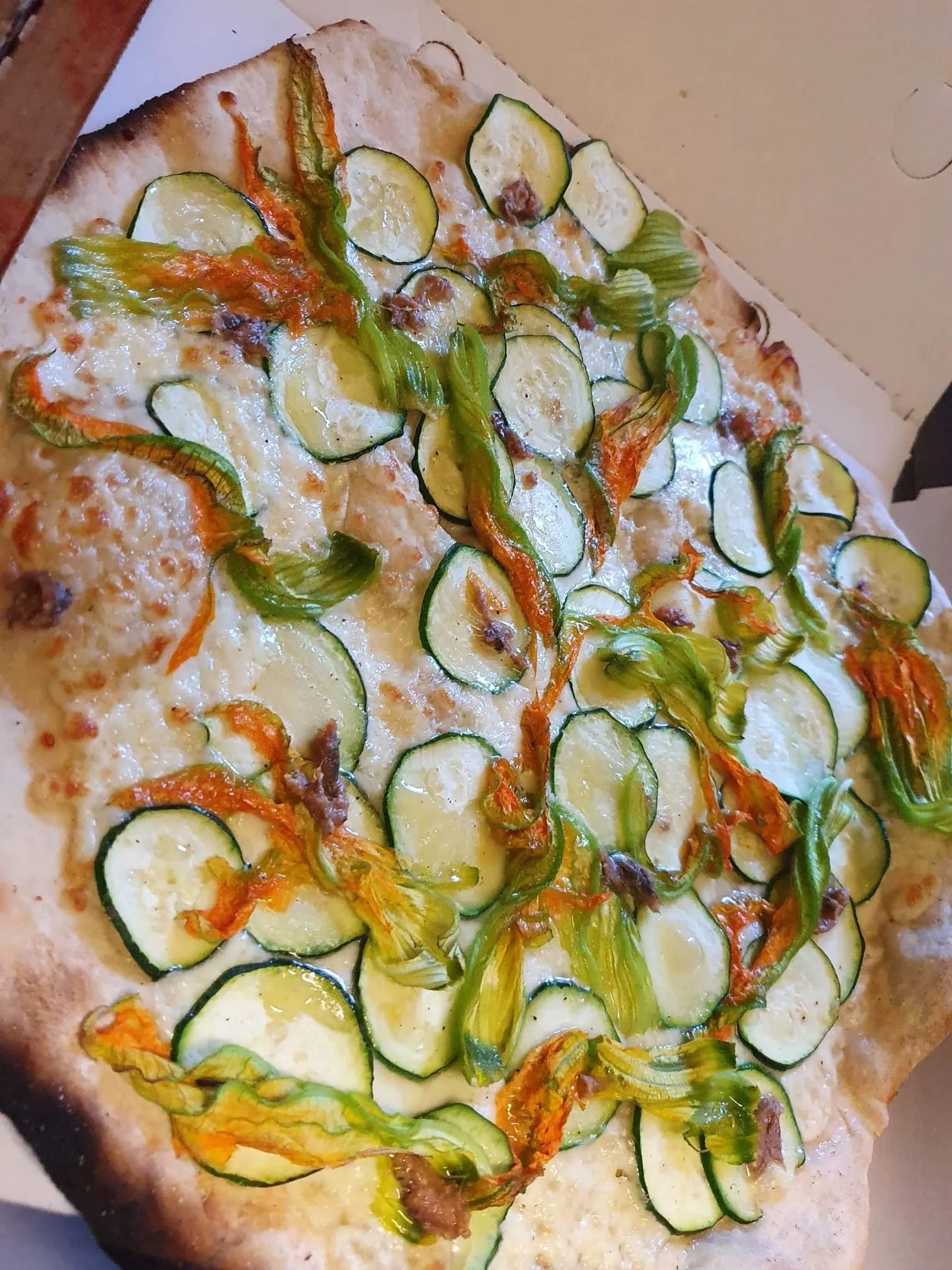 Pizza con zucchine, servita su un vassoio di cartone, con formaggio fuso ed erbe aromatiche.