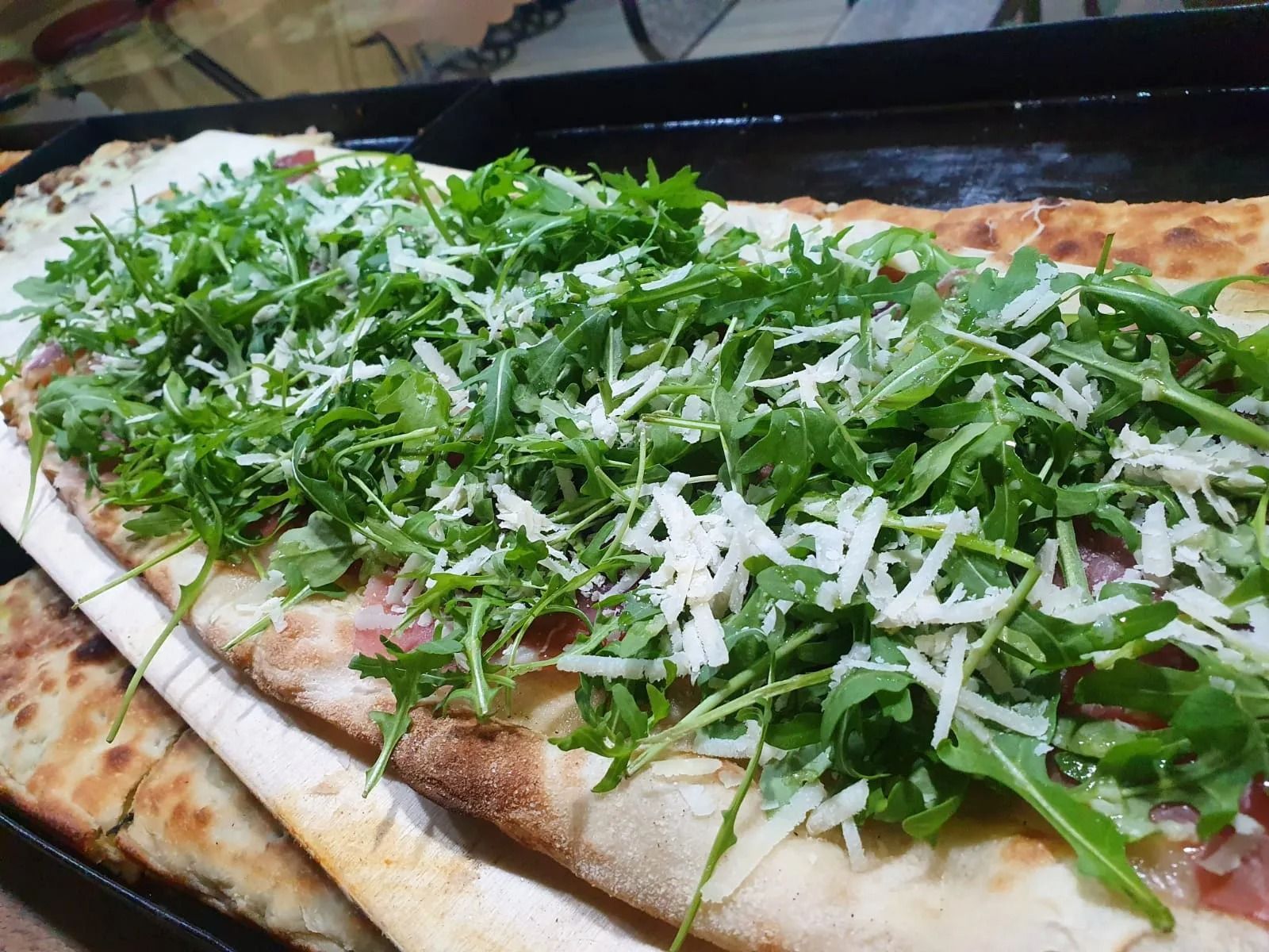 Pizza sottile con rucola e formaggio grattugiato, appena sfornata.