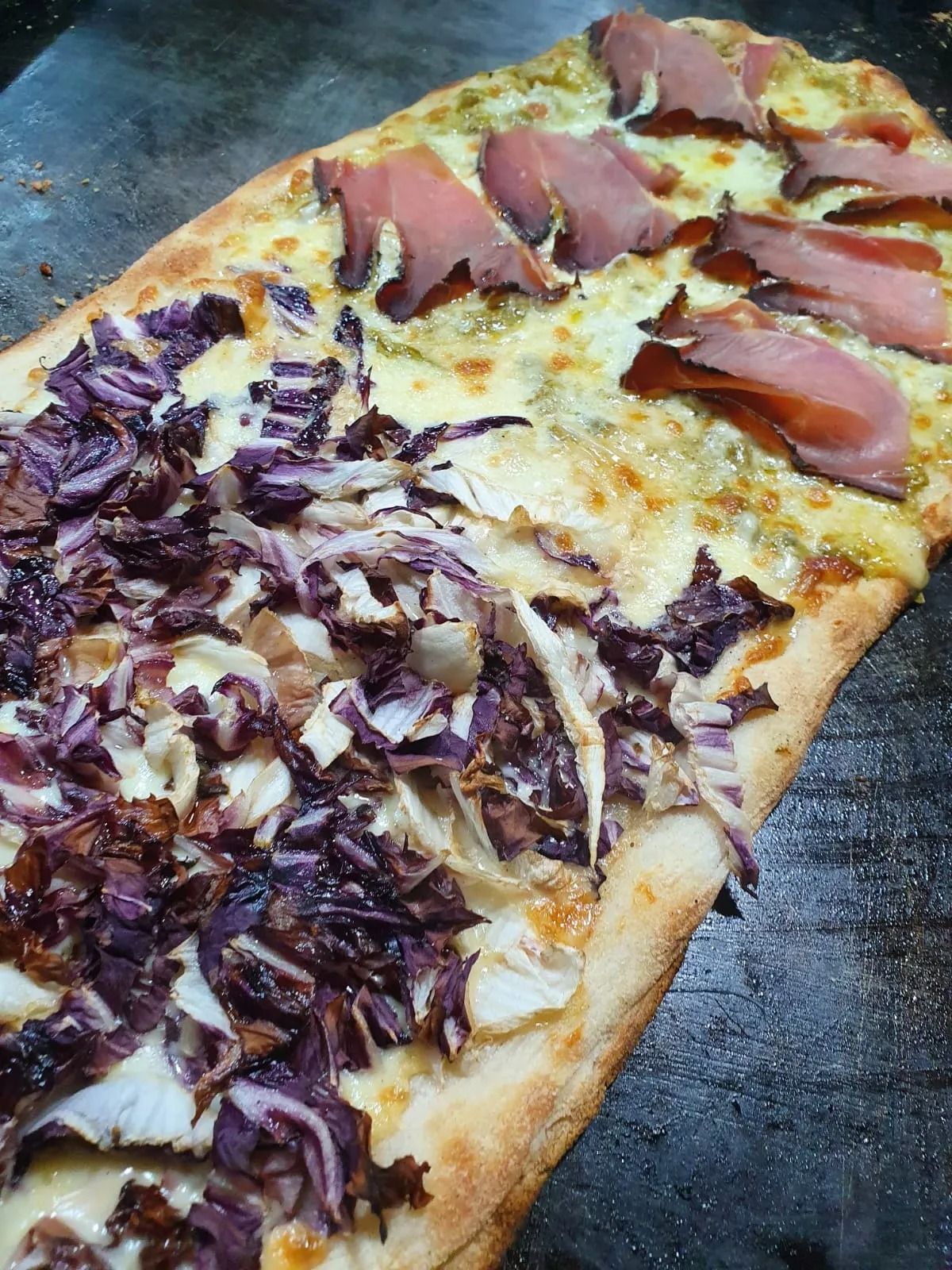 Primo piano di una fetta di pizza condita con cavolo rosso e prosciutto su un vassoio