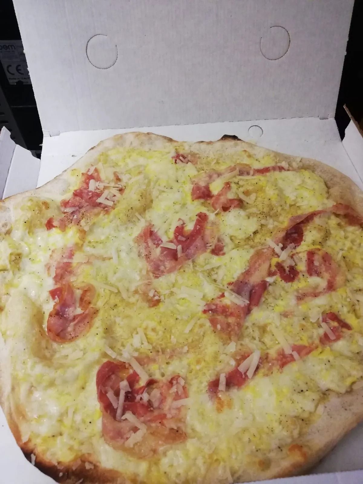Scatola della pizza aperta con una pizza al formaggio e prosciutto su un rivestimento di cartone.