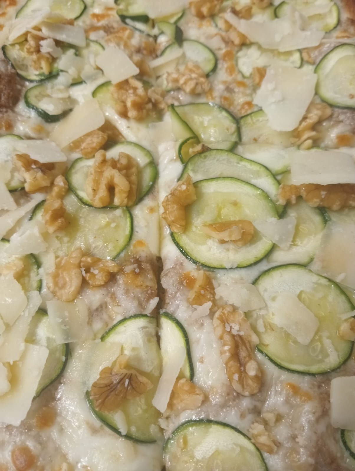Primo piano di una pietanza al forno con zucchine e noci, con salsa cremosa e crosticina dorata.