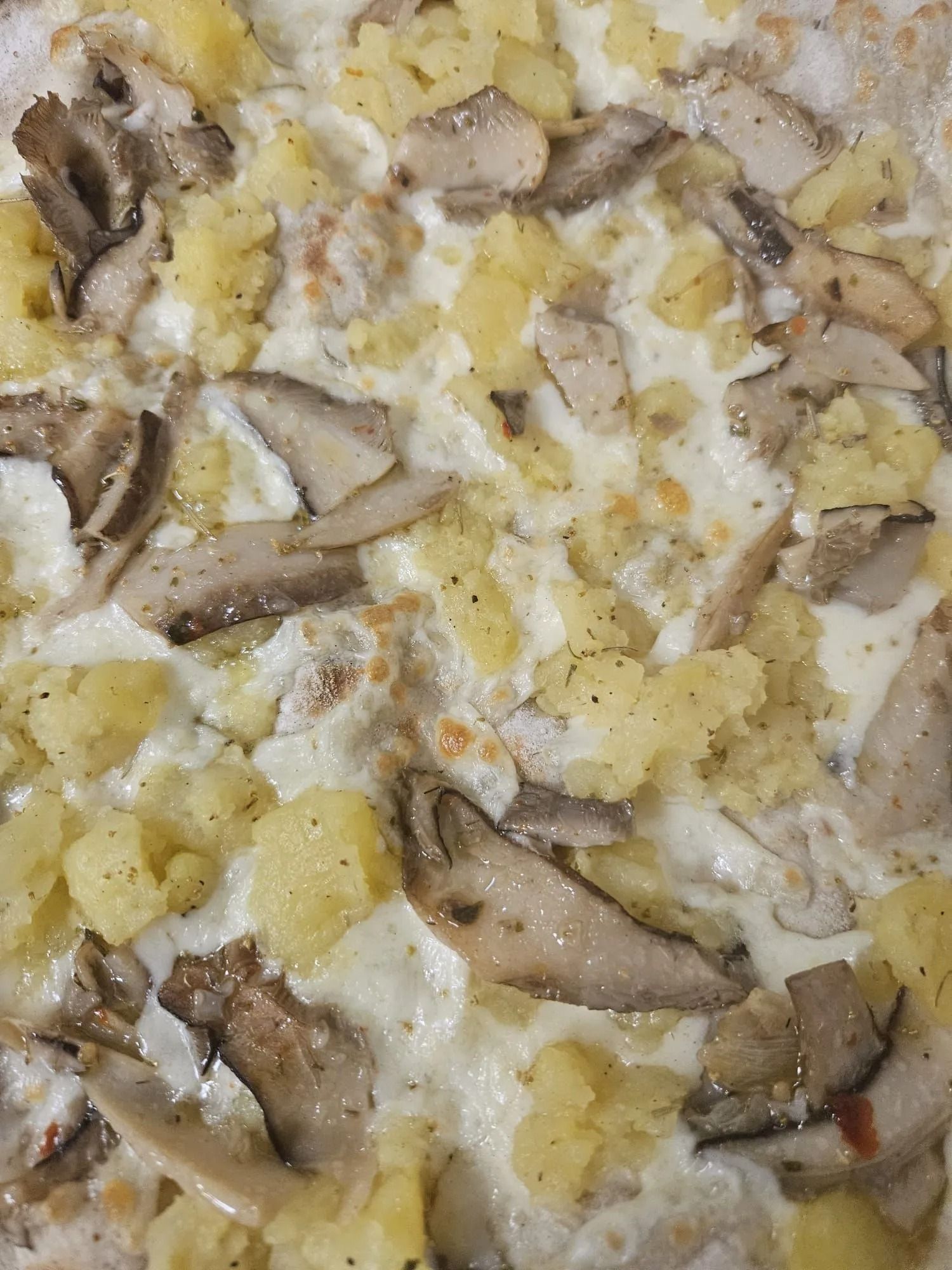 Primo piano di un cremoso piatto di patate e funghi con formaggio fuso in cima.