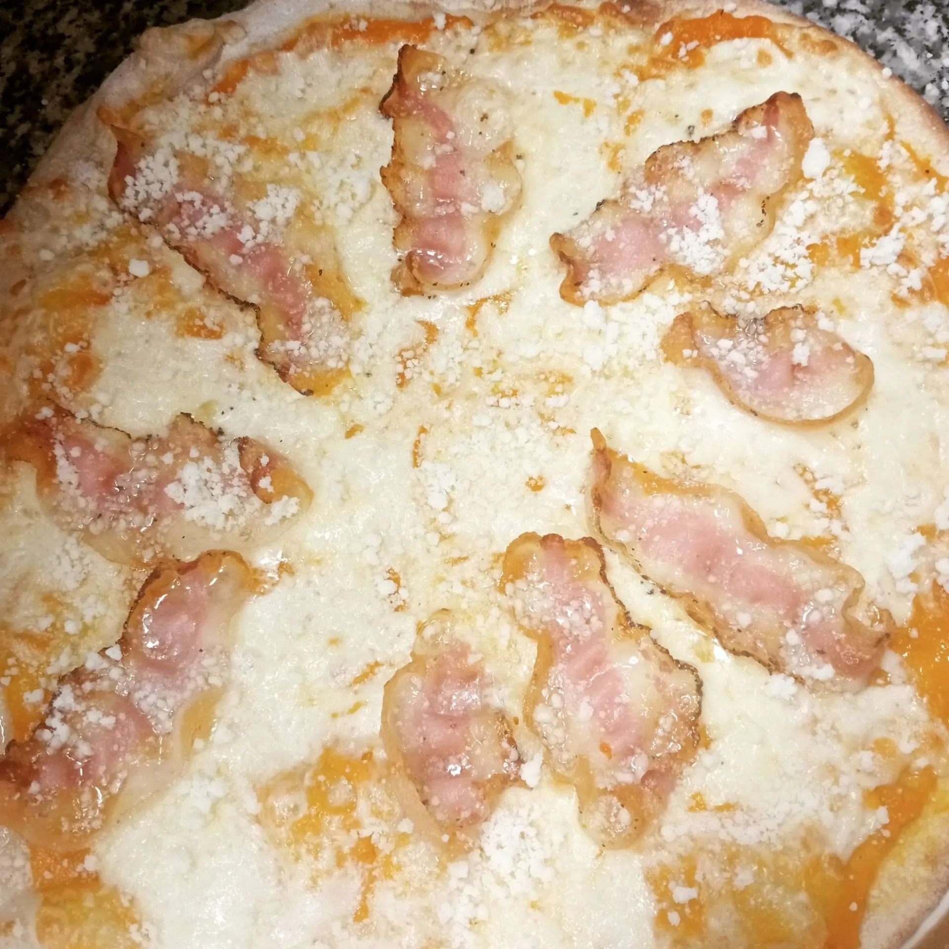 Primo piano di una pizza al formaggio con pezzetti di pancetta o prosciutto rosa e crosta dorata e fusa.