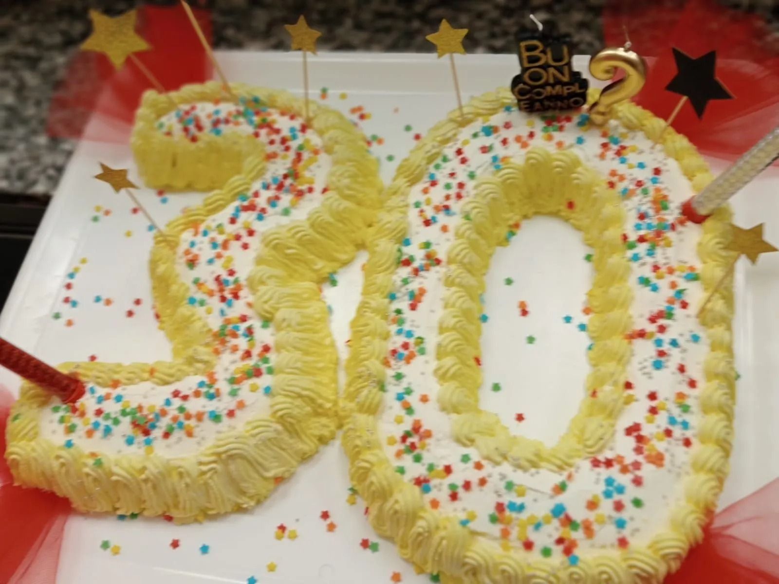 Torta per il 30° compleanno con numeri di glassa gialla, zuccherini colorati e candeline su un tavolo bianco.