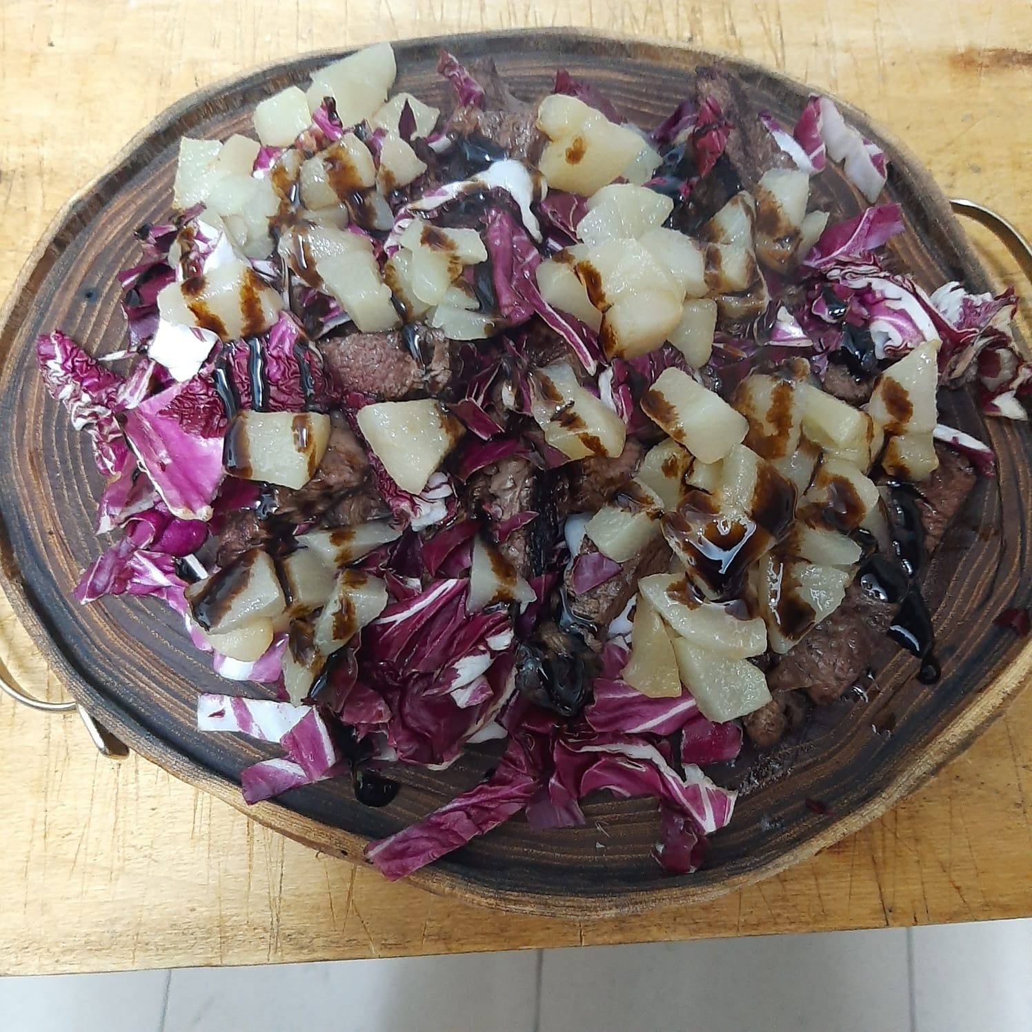 Piatto di legno con radicchio tritato, patate a dadini e glassa di aceto balsamico.