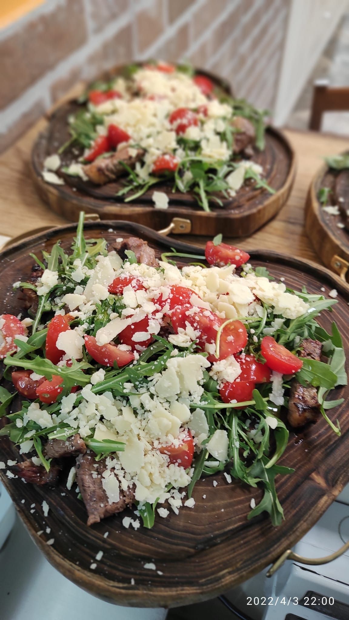 Piatti di insalata con verdure miste, pomodorini, feta e formaggio grattugiato su un tavolo di legno.