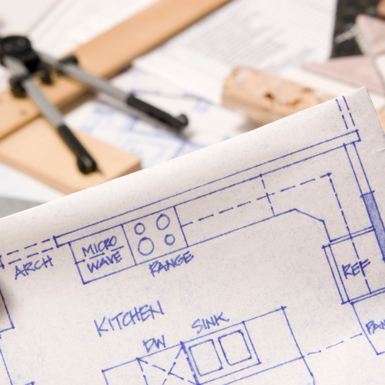 Blue architectural kitchen floor plan on paper with drafting tools in the background.