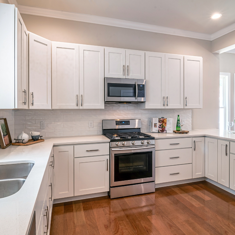 Modern kitchen with white cabinets, stainless steel appliances, white subway tile backsplash, and polished wood floors.