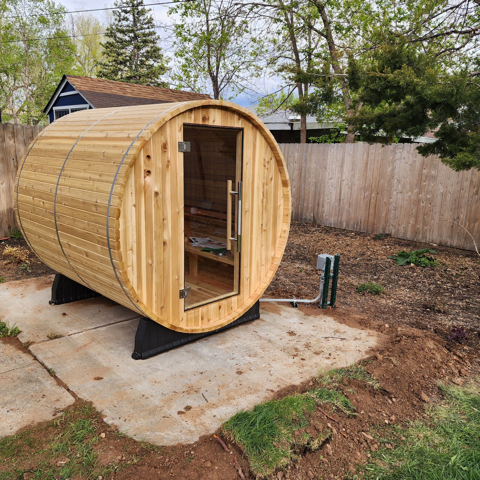 A wooden barrel sauna is sitting in the backyard of a house.