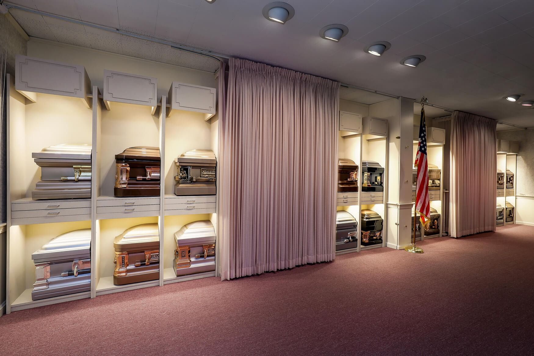 Interior of a formal hall with curtained alcoves displaying stacked folded textiles and an American flag at right.
