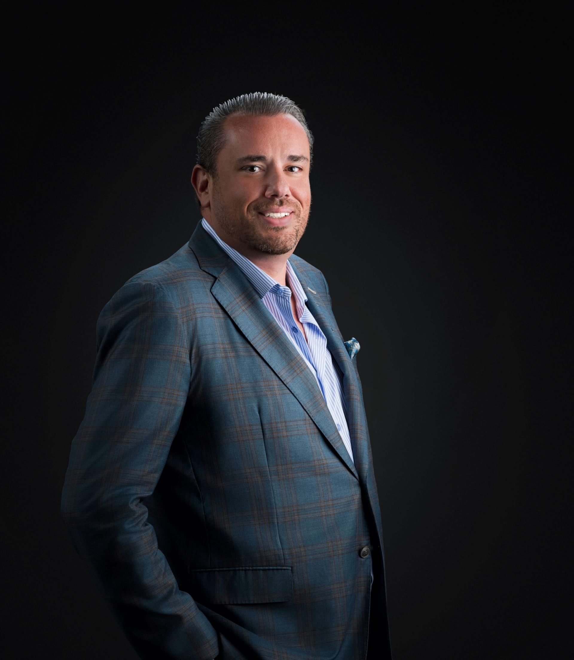 Man in a blue suit smiling against a dark background