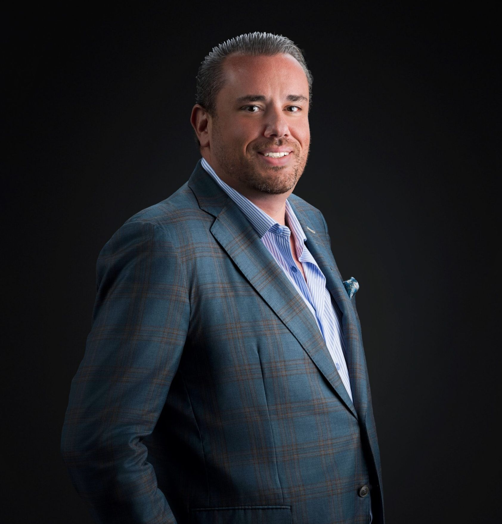 Man in a blue suit smiling against a dark background