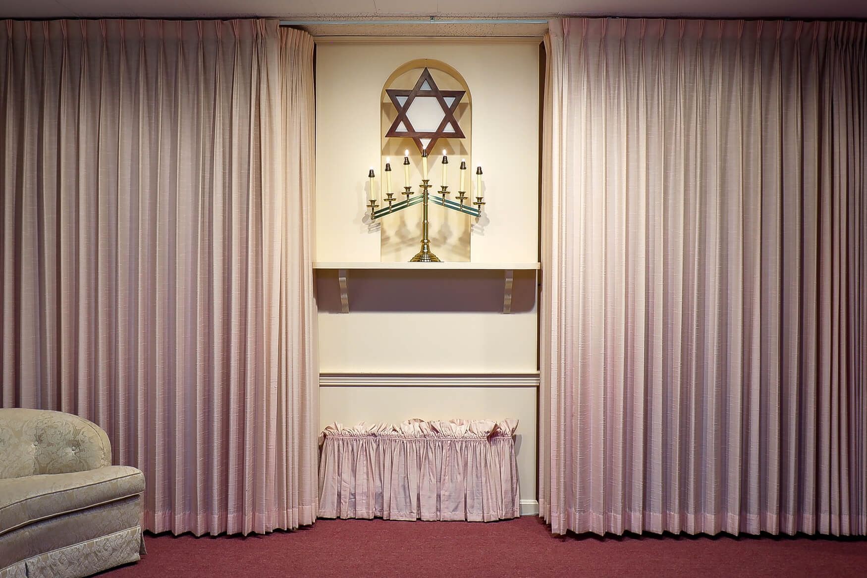 Curtained stage with Star of David and candelabrum, pink carpet, and a sofa at left