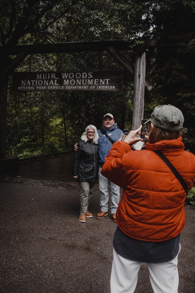 People posing by the Hilli Woods National Monument sign in a forested entrance.