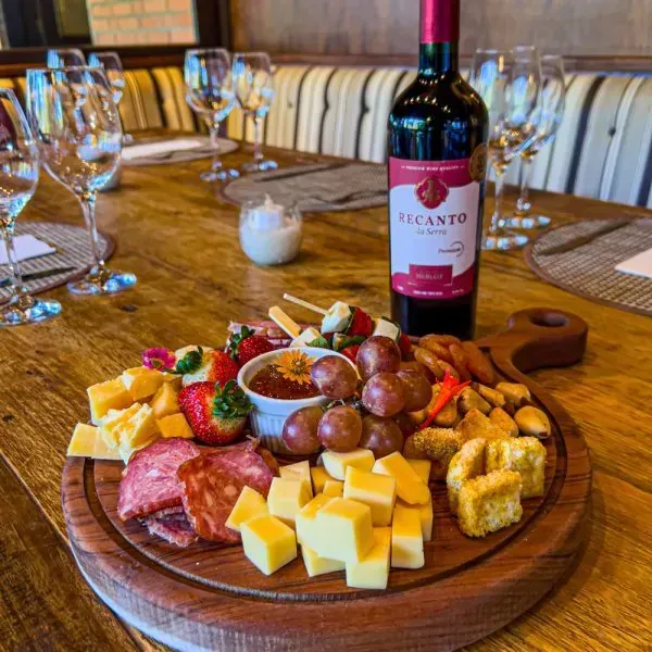 Tábua de charcutaria com queijo, frutas, biscoitos e vinho em uma mesa de restaurante.