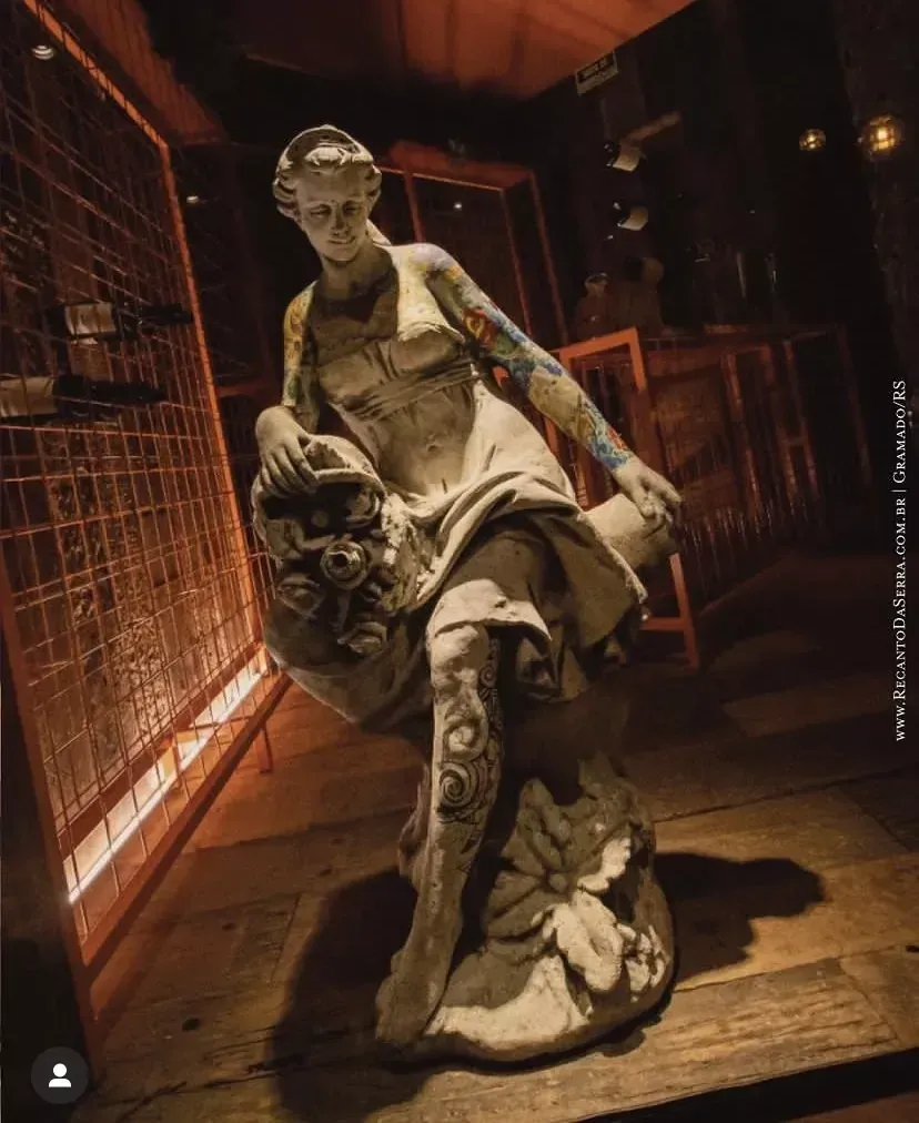 Estátua de mármore de uma figura sentada em uma exposição de museu com iluminação tênue e aconchegante em tons de laranja.
