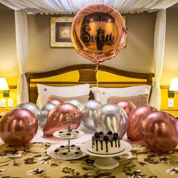 Quarto de aniversário decorado com balões dourados rosê, um balão com o nome "Sofia" e um bolo na cama.