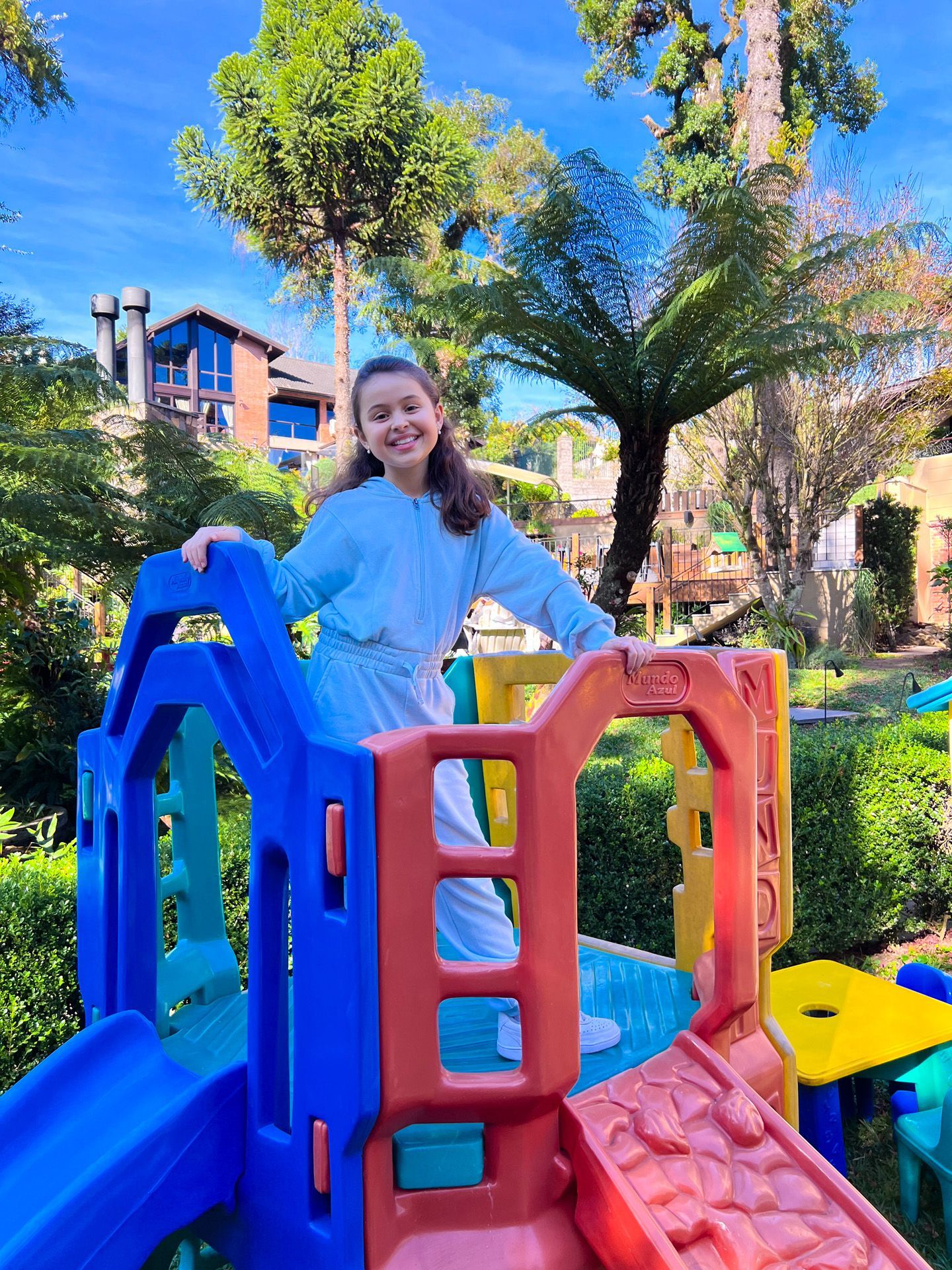 Pessoa sorrindo em um brinquedo colorido de um parquinho em um parque ensolarado.