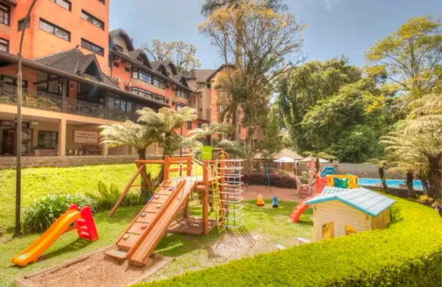 Parque infantil com escorregadores e estruturas para escalada ao lado de um hotel.