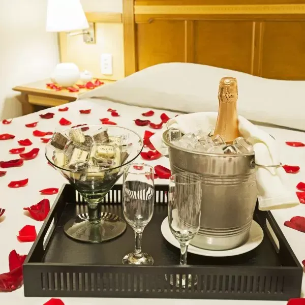 Balde de champanhe com taças e dinheiro sobre uma cama coberta de pétalas de rosa vermelha.