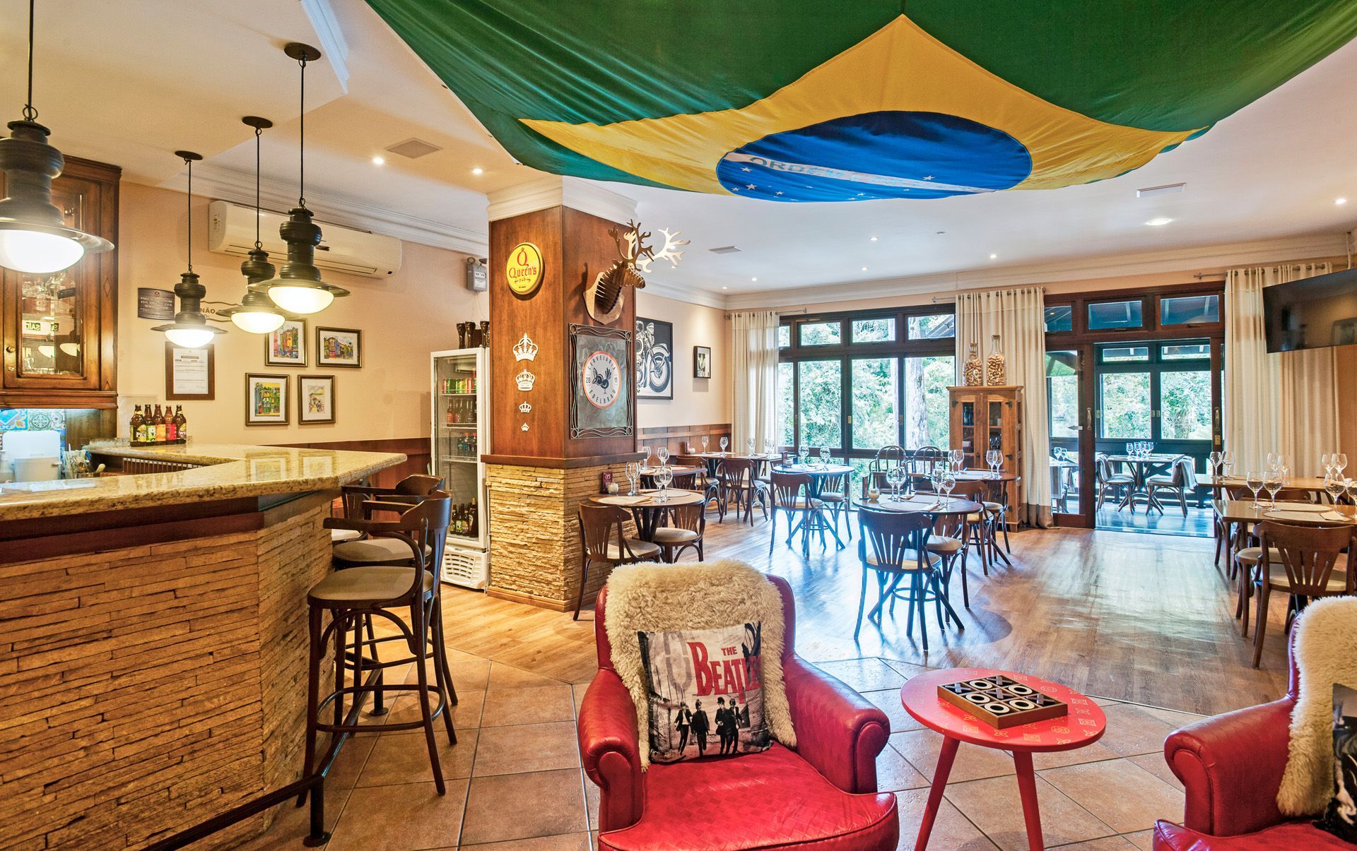 Interior aconchegante de café com cadeiras de vime, banquetas, luminárias pendentes e tecido colorido drapeado no teto.