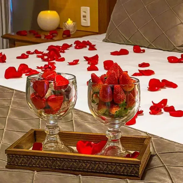Morangos em taças de vidro sobre uma cama de pétalas de rosa e uma bandeja para velas.