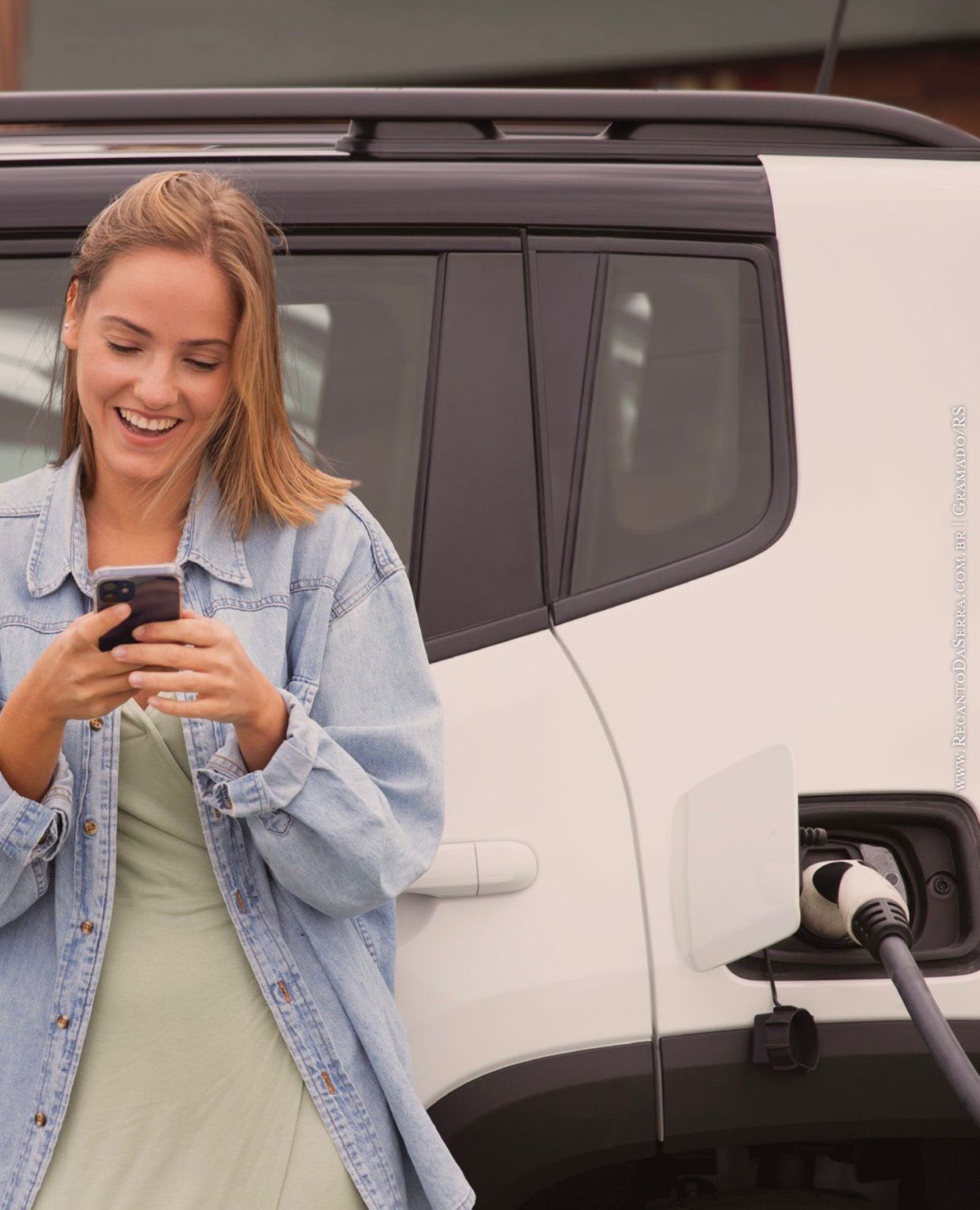 Mulher carregando um SUV elétrico enquanto sorri para o celular.