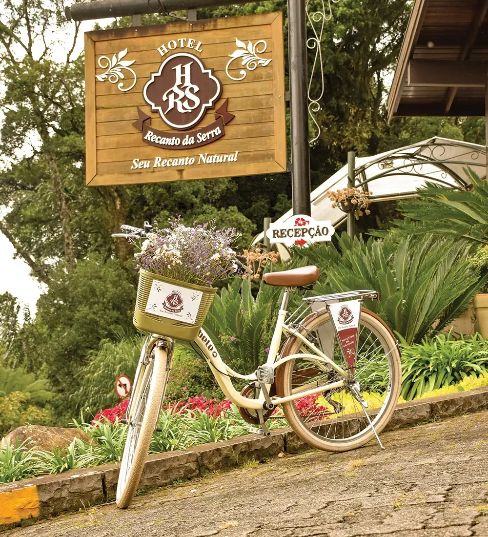 Bicicleta decorativa branca ao lado de uma placa de madeira de um café em um jardim exuberante.