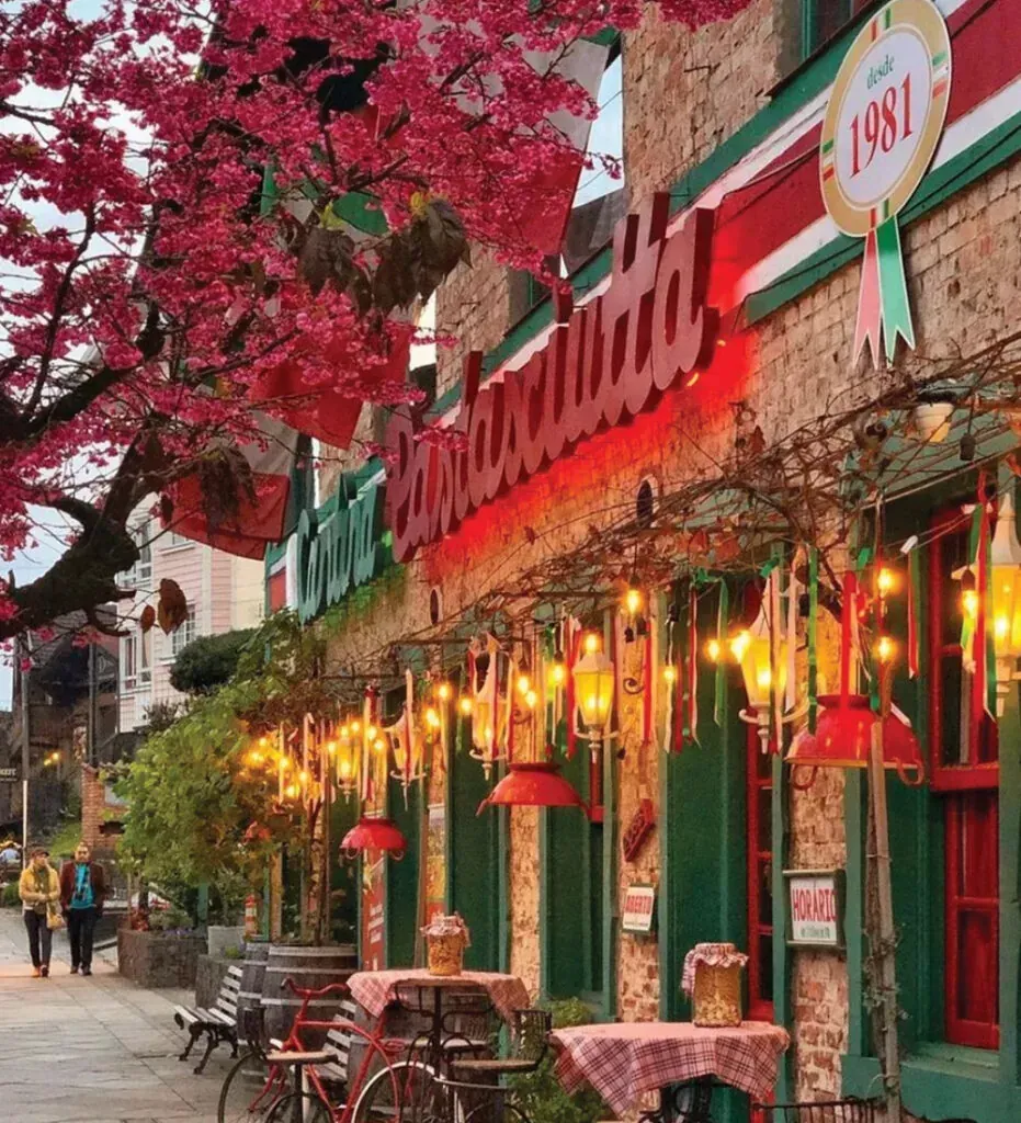 Charmoso café de rua com toldos vermelhos, lanternas brilhantes, detalhes em verde e árvores com folhas vermelhas de outono.