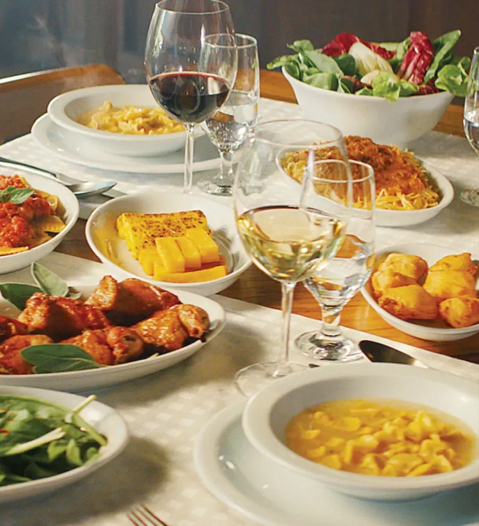 Uma mesa posta com pratos variados, saladas, pãezinhos, sopa e taças de vinho para uma refeição.