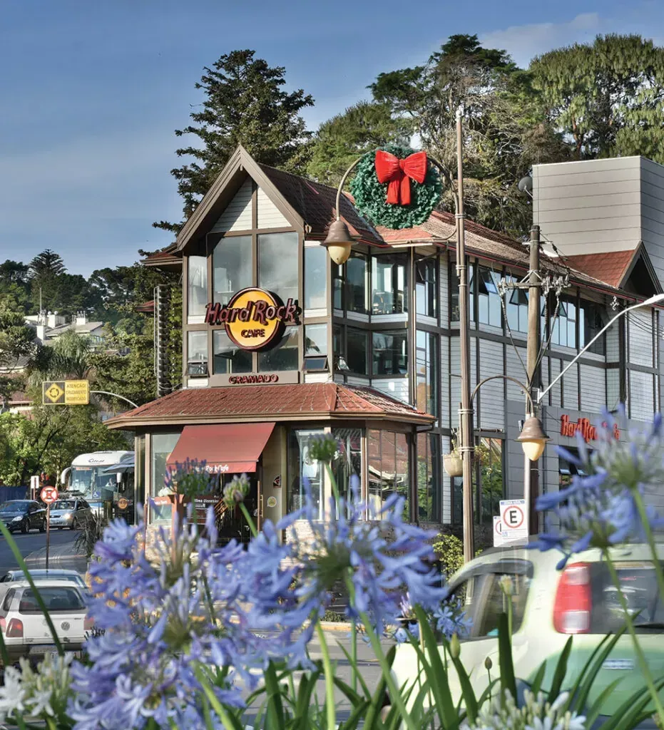 Rua encantadora com um prédio em estilo Tudor, decoração com laços vermelhos e flores roxas em primeiro plano.