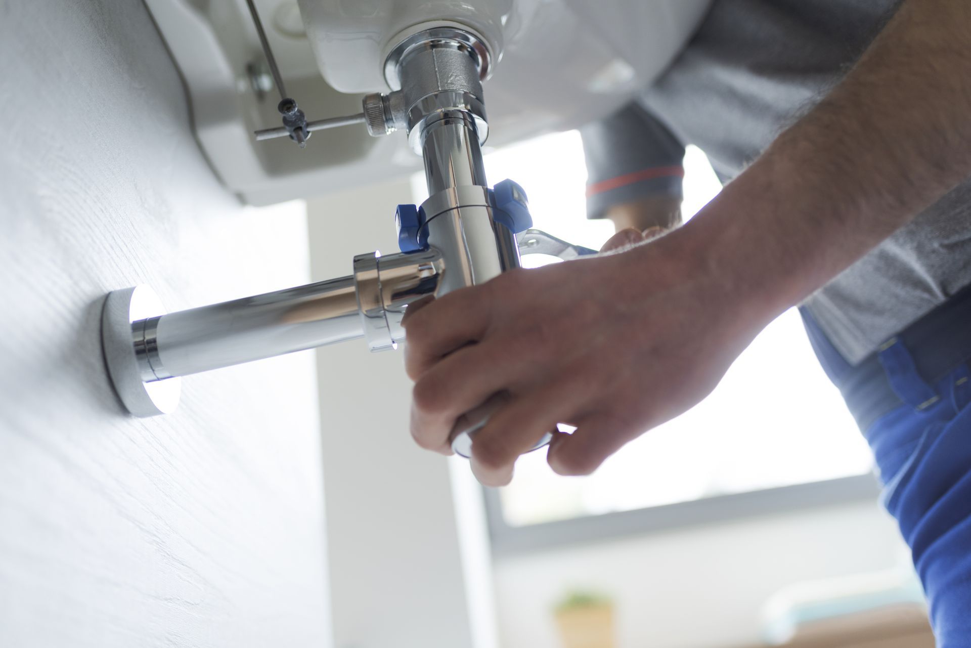 Plumber working under a sink, tightening a pipe with a wrench.