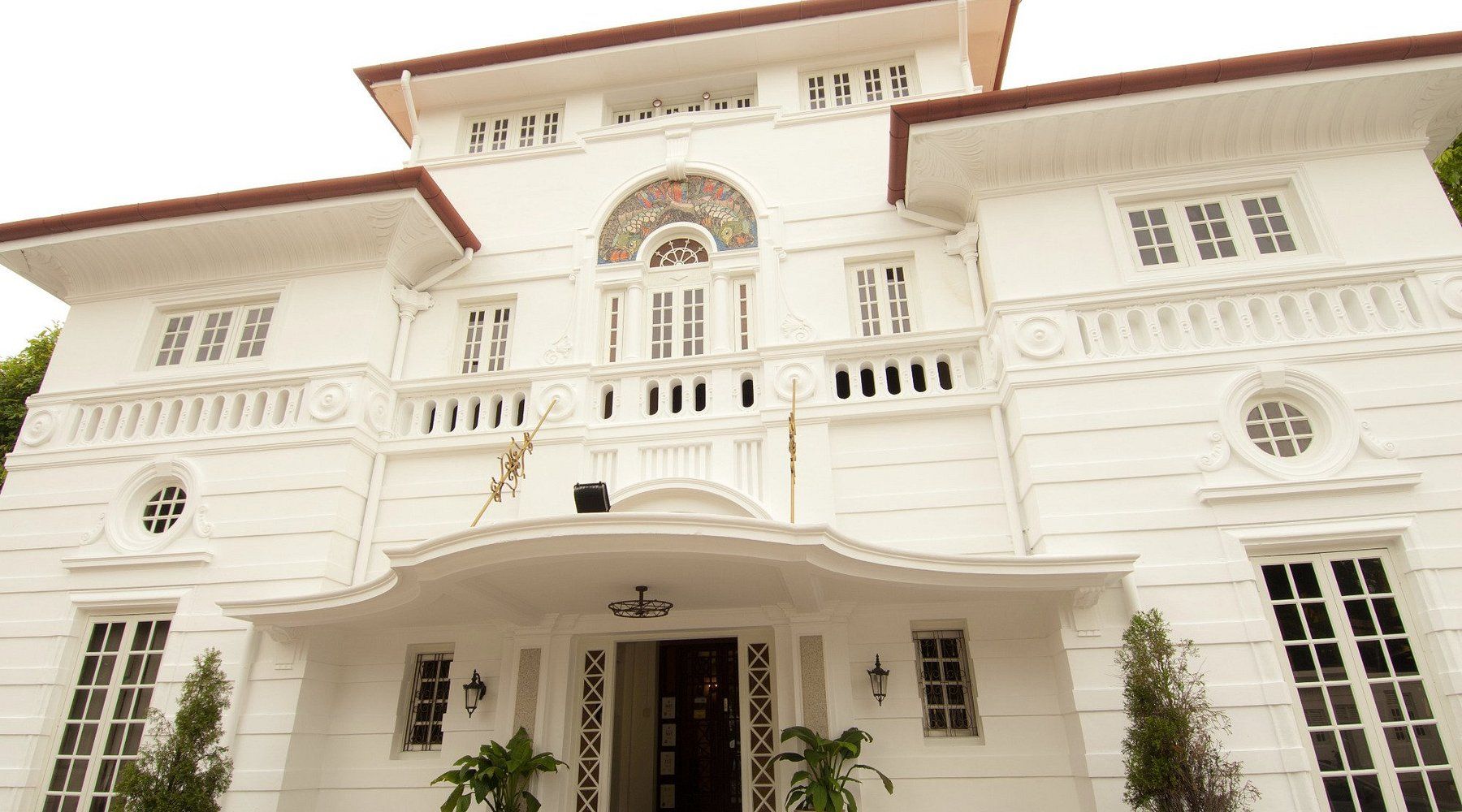 White two-story house with columns and balconies. Front entrance under a curved overhang, large windows.