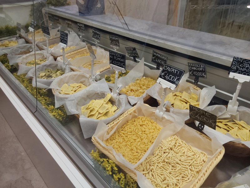 Varietà di pasta in cestini esposti sotto un bancone di vetro in un mercato.