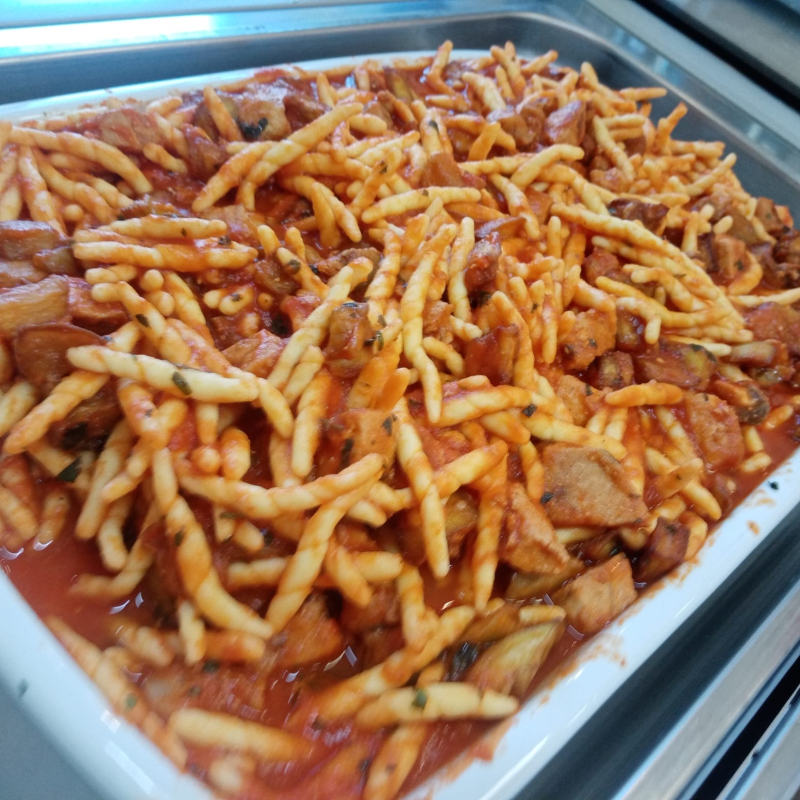 Pasta con sugo di pomodoro, pezzi di carne ed erbe aromatiche, servita in un piatto bianco.