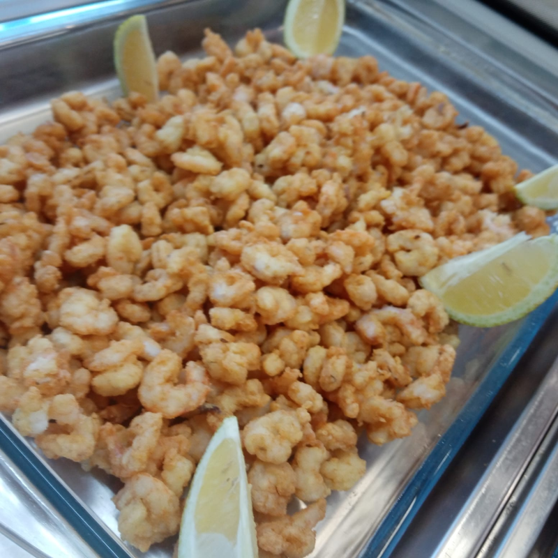 Gamberi popcorn fritti su un piatto con spicchi di limone.
