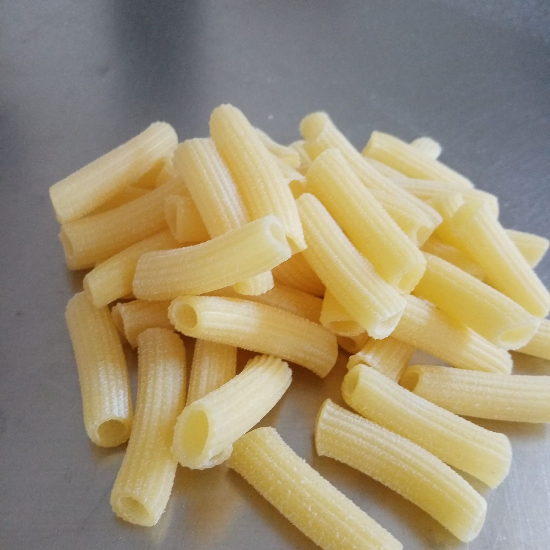 Mucchio di penne crude su una superficie lucida.