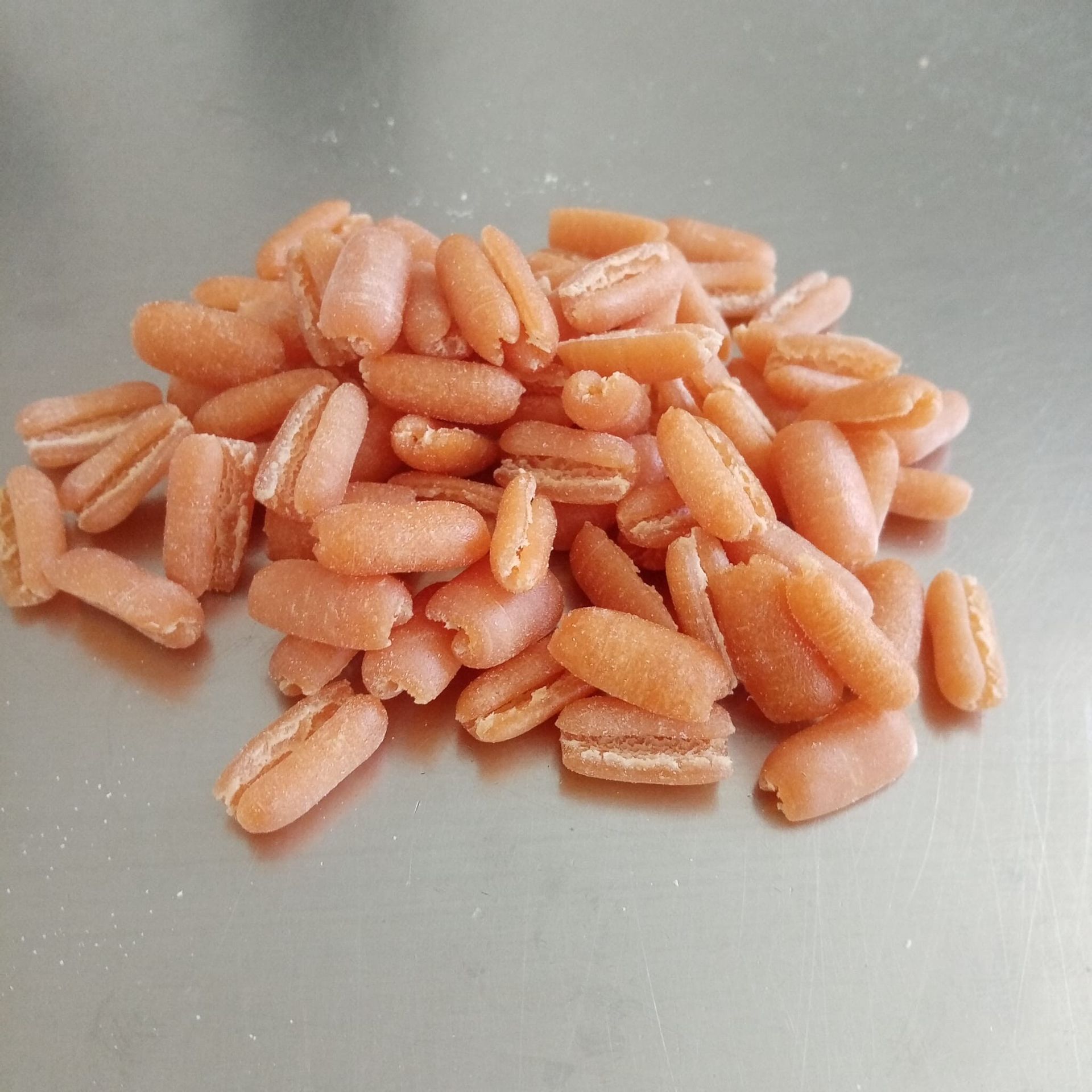 Mucchio di formati di pasta rosa, probabilmente garganelli, su una superficie metallica.