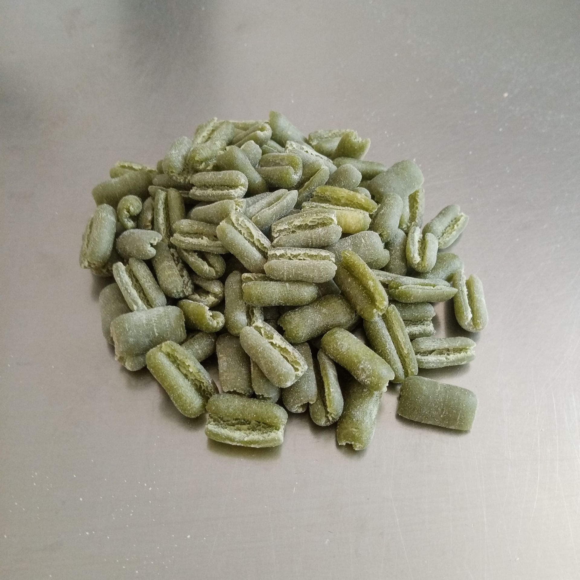 Gnocchi di pasta verde ammucchiati su una superficie argentata.