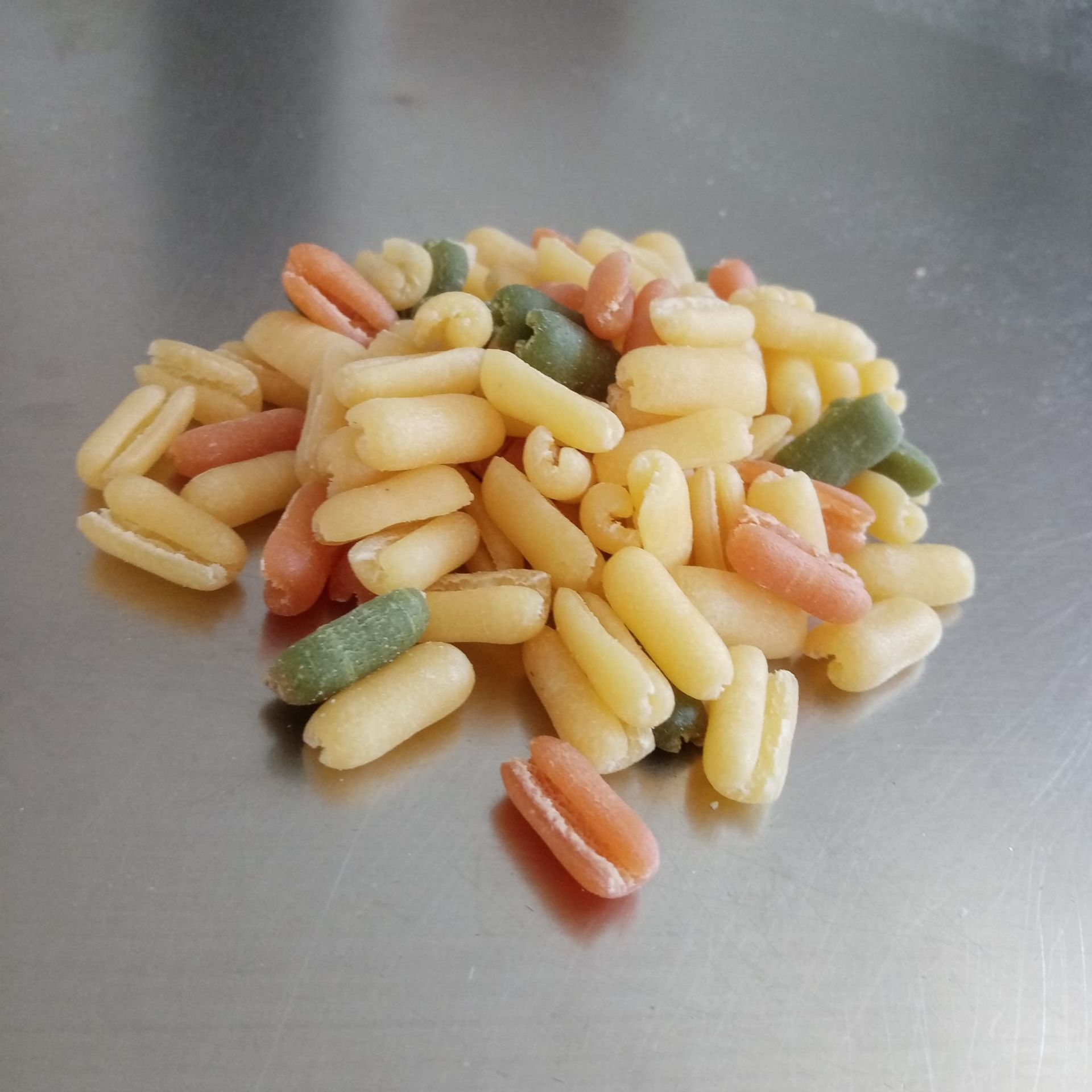 Mucchio di pasta cavatelli tricolore su una superficie argentata lucida.