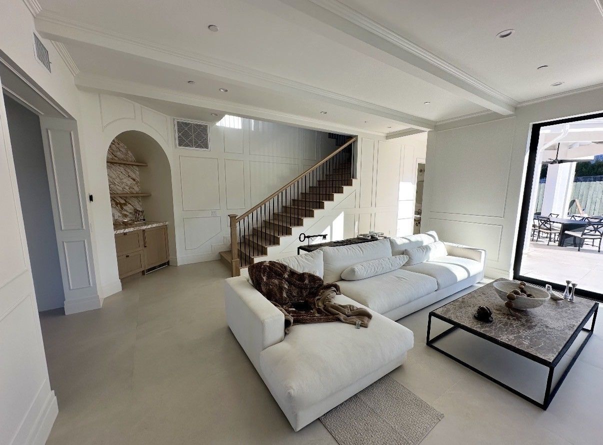 Bright open living room with white sectional sofa, black coffee table, and staircase in the background